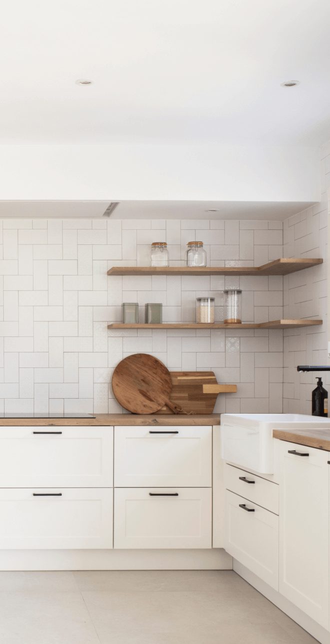 Cocina blanca con baldas de madera, azulejos rectangulares y encimera de madera en vivienda de la Costa Brava.