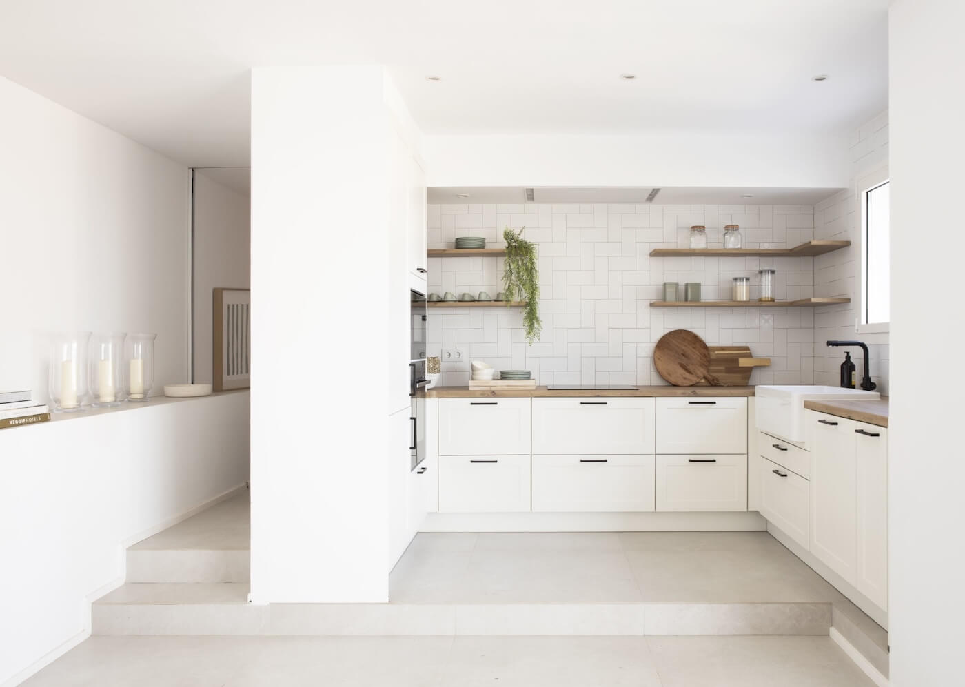 Cocina blanca de estilo mediterráneo con estanterías de madera y luz natural en casa de la Costa Brava.