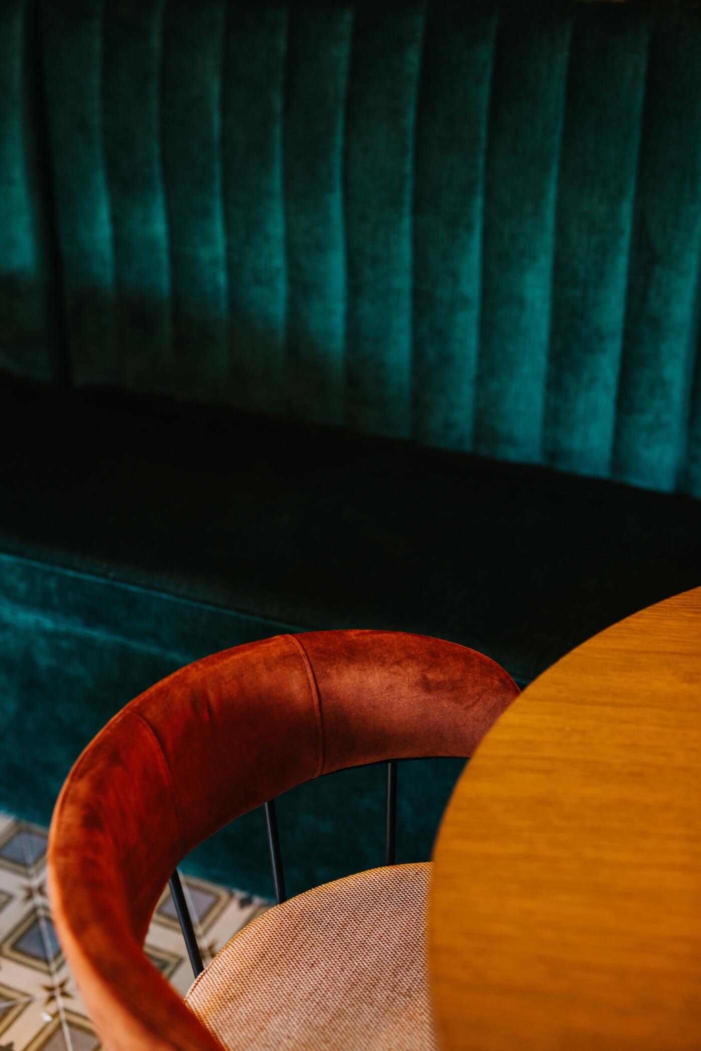 Detalle de silla de terciopelo rojo y banqueta tapizada en verde en el restaurante Casa Petra, Barcelona.
