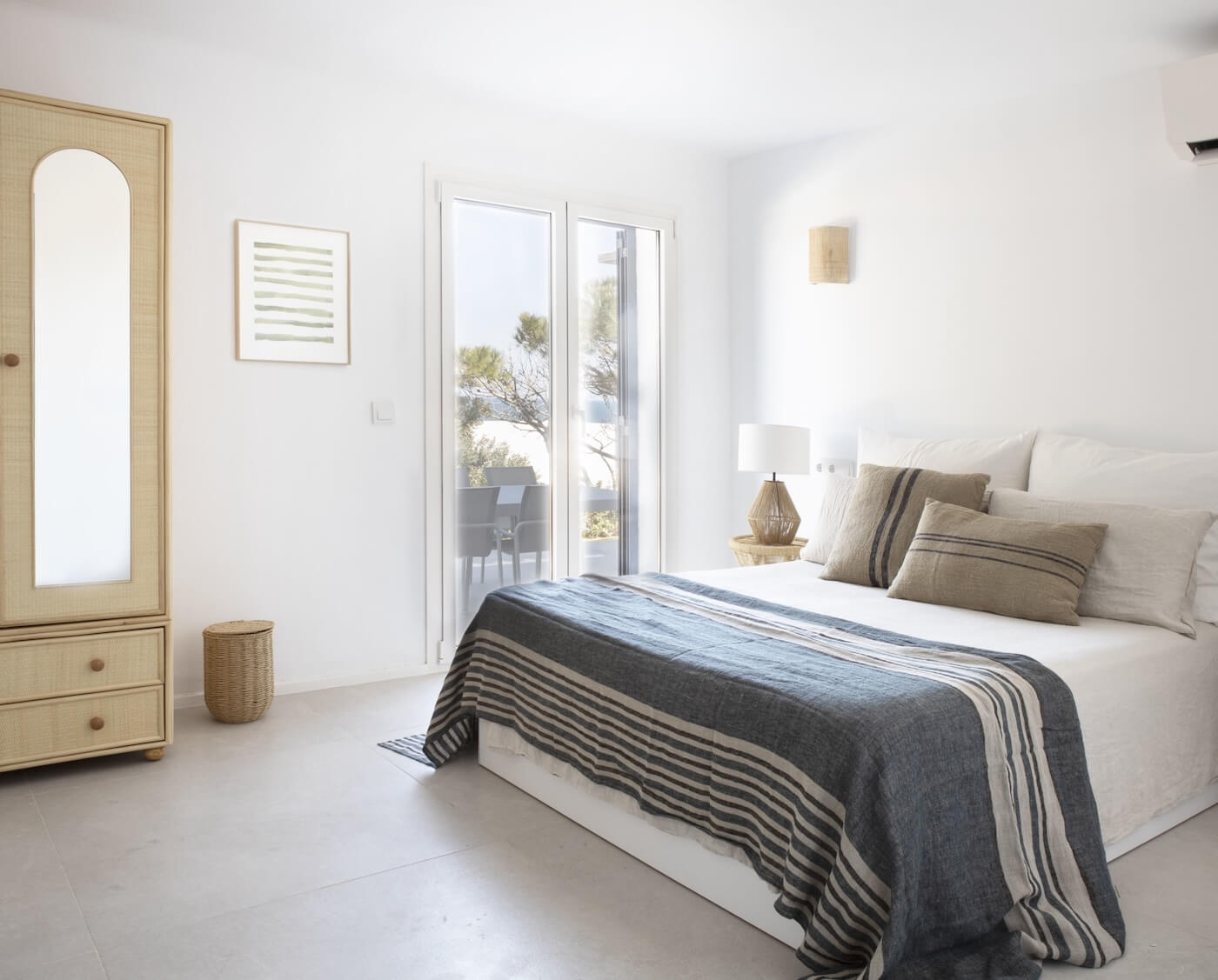 Dormitorio de estilo mediterráneo en casa de la Costa Brava, con textiles naturales, mobiliario en fibras y luz exterior.