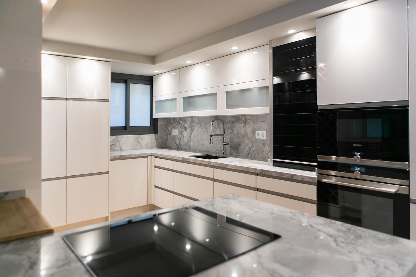 Cocina moderna en forma de L con mobiliario blanco, encimeras de granito y grifería de diseño.