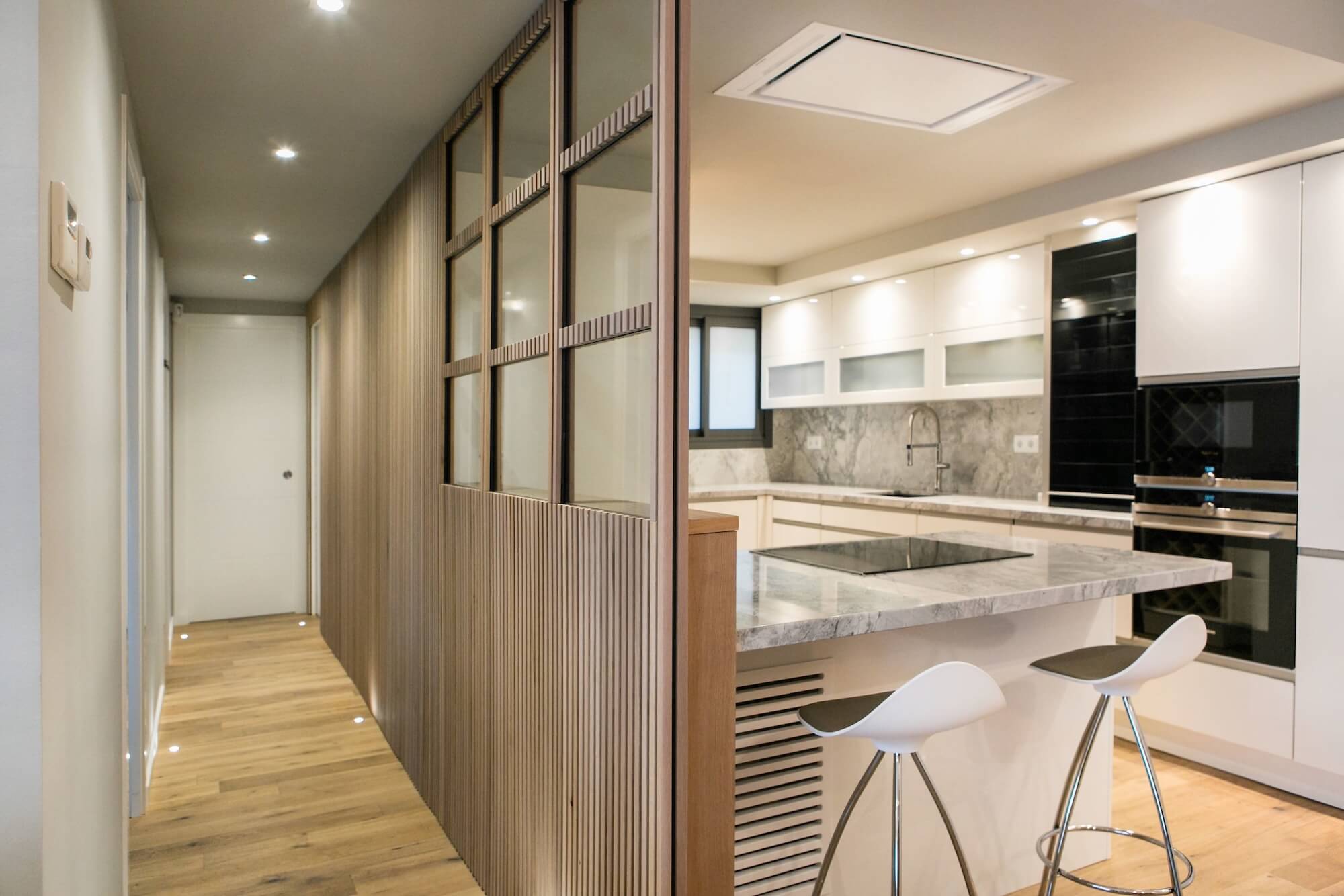 Cocina moderna con isla de mármol, panelado de madera con cristaleras y electrodomésticos integrados.