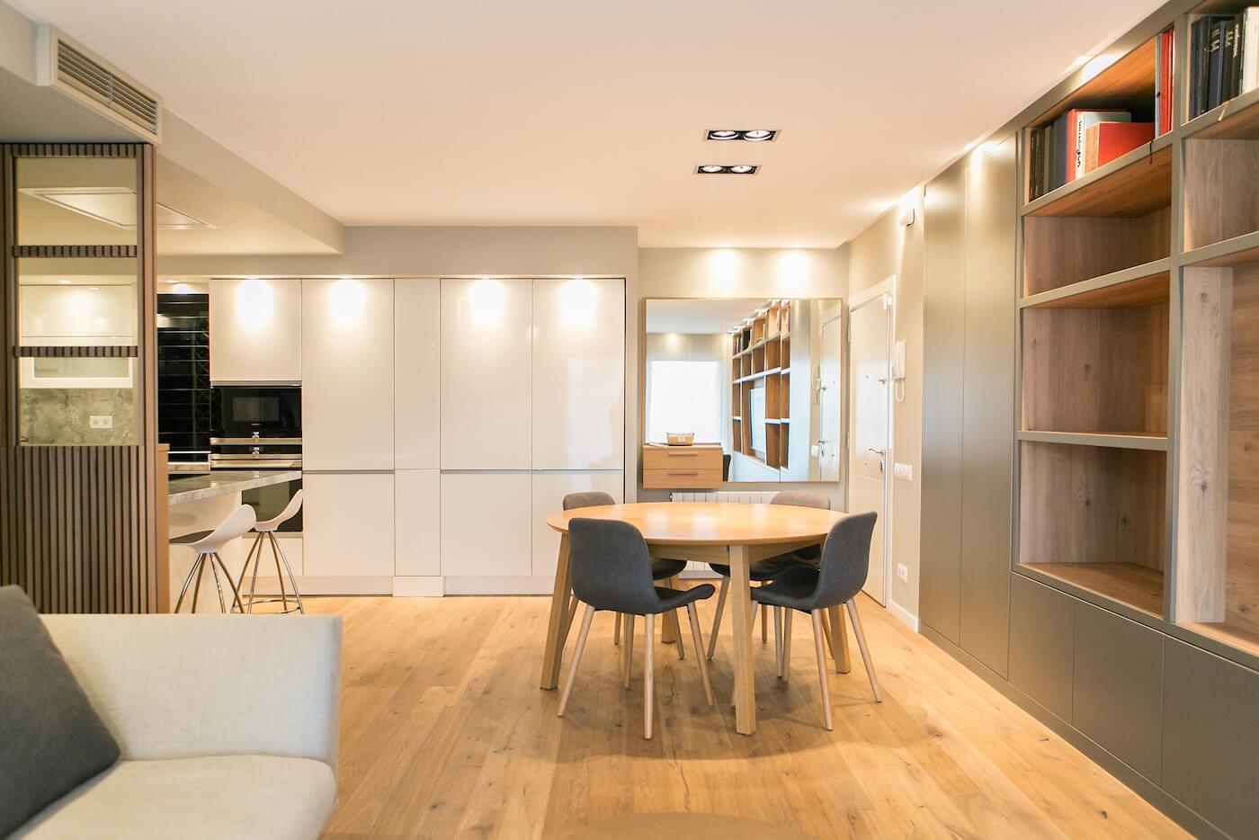 Comedor con mesa redonda de madera, sillas tapizadas y estanterías a medida en un salón reformado.