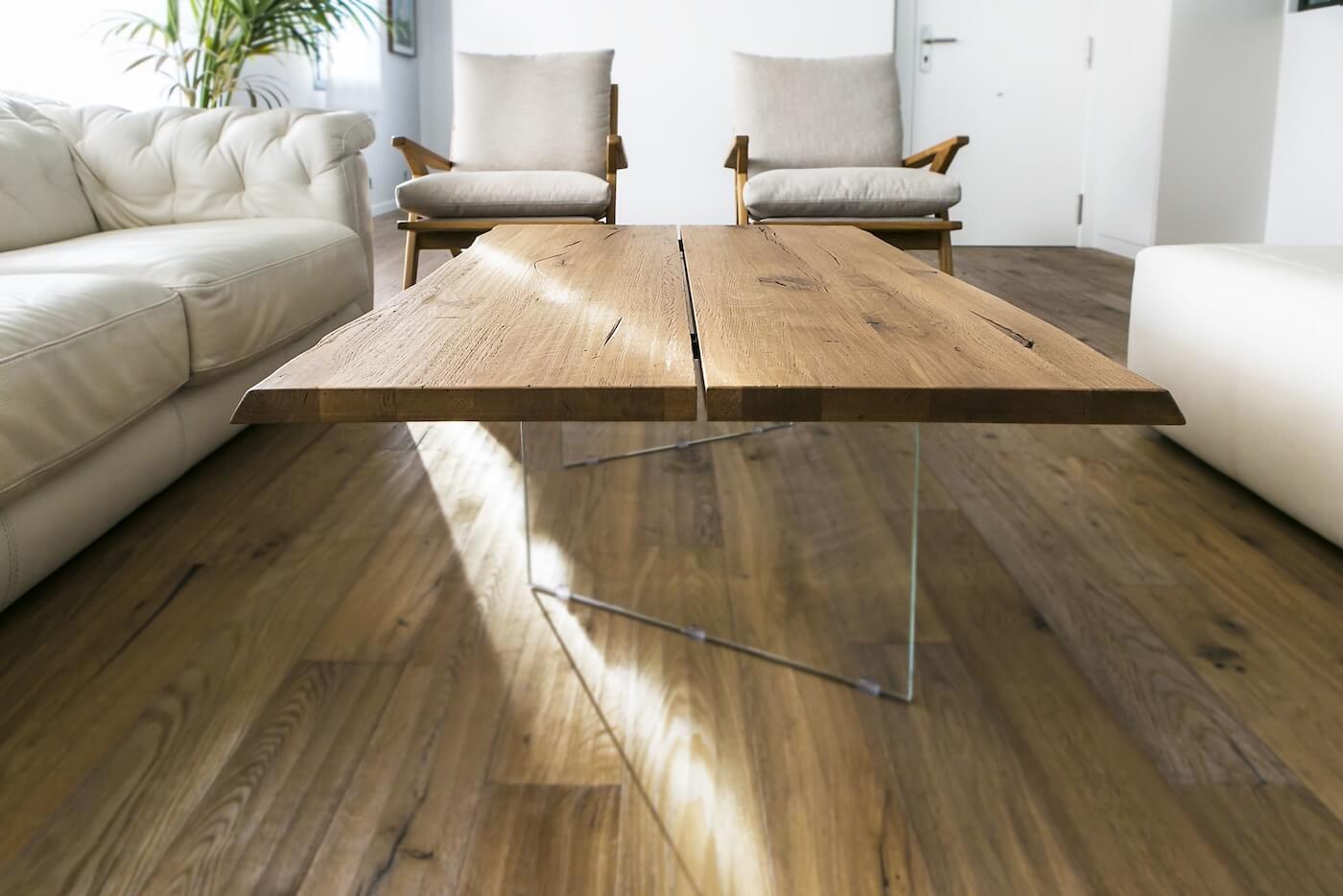 Mesa de centro en madera natural con patas de vidrio, rodeada de sofás tapizados y sillones de madera en salón de piso reformado en Sabadell.