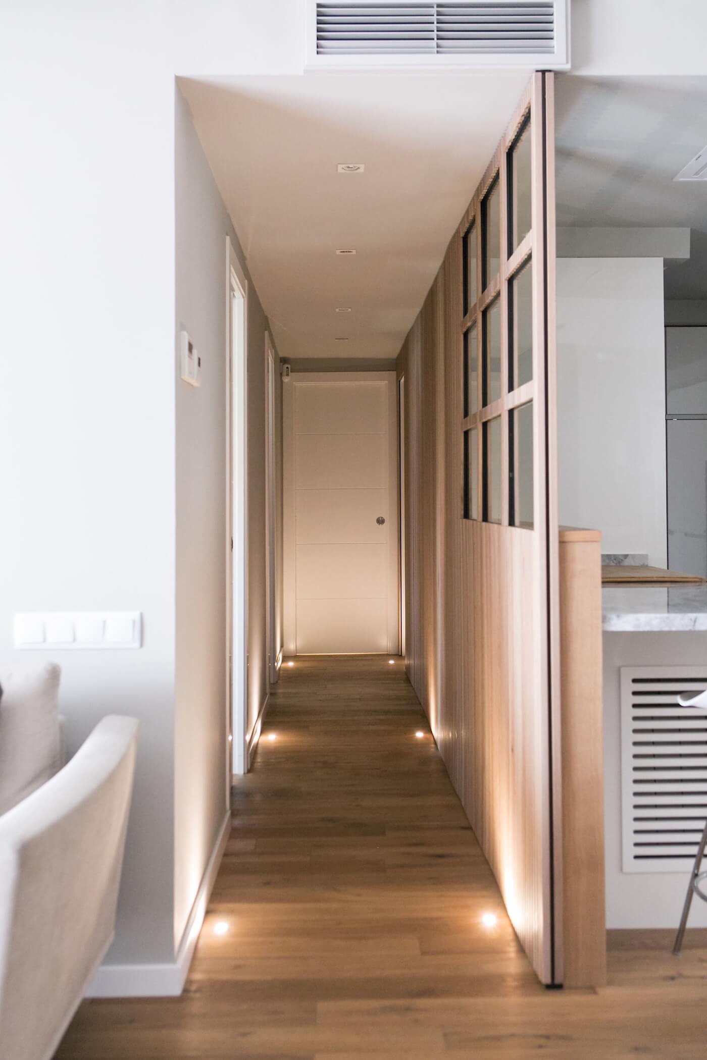 Pasillo con suelo de madera natural e iluminación LED empotrada en una vivienda reformada en Gran Vía, Barcelona.
