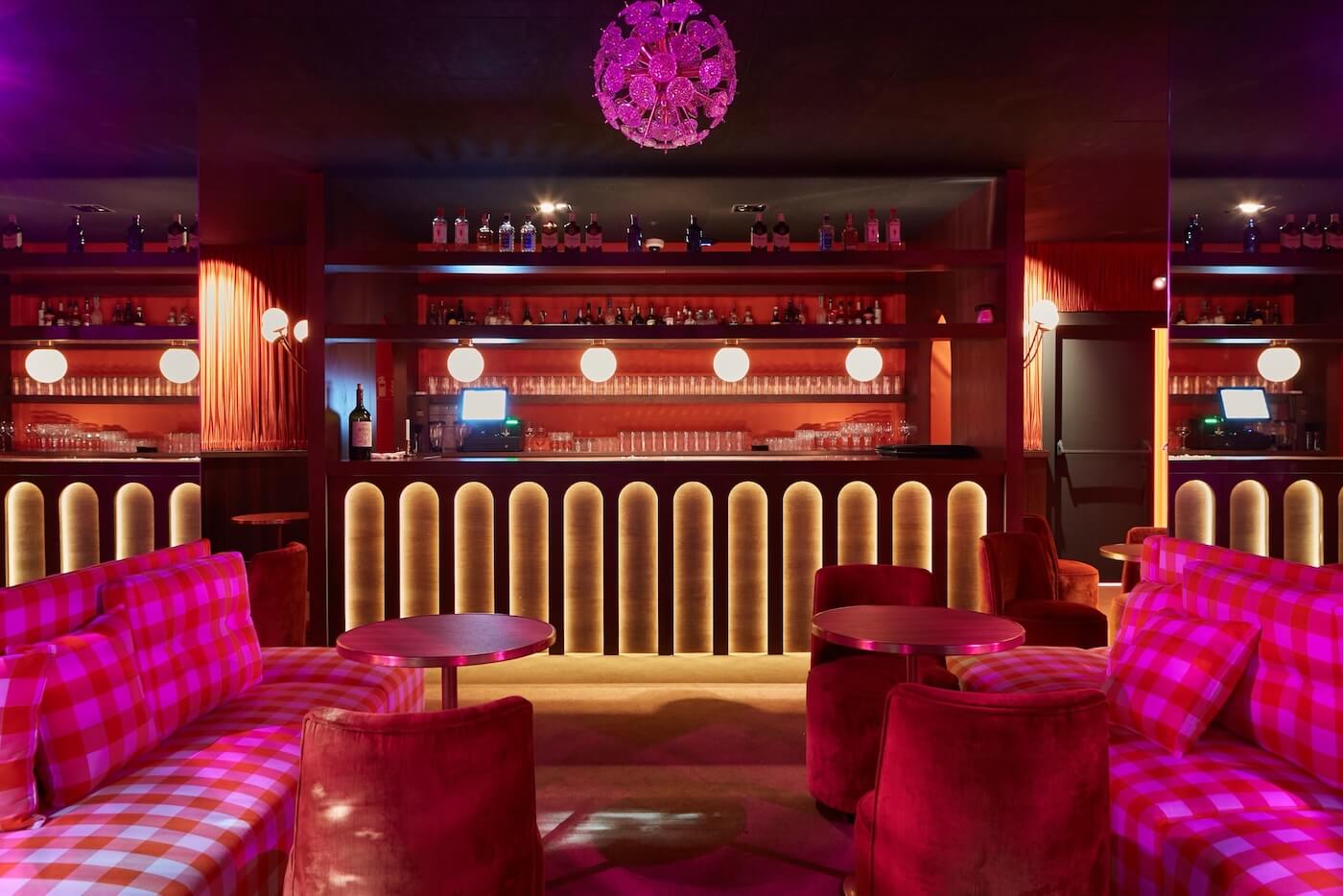 Bar del restaurante Gala con iluminación escenográfica, sofás a cuadros rojos y mobiliario tapizado en terciopelo.