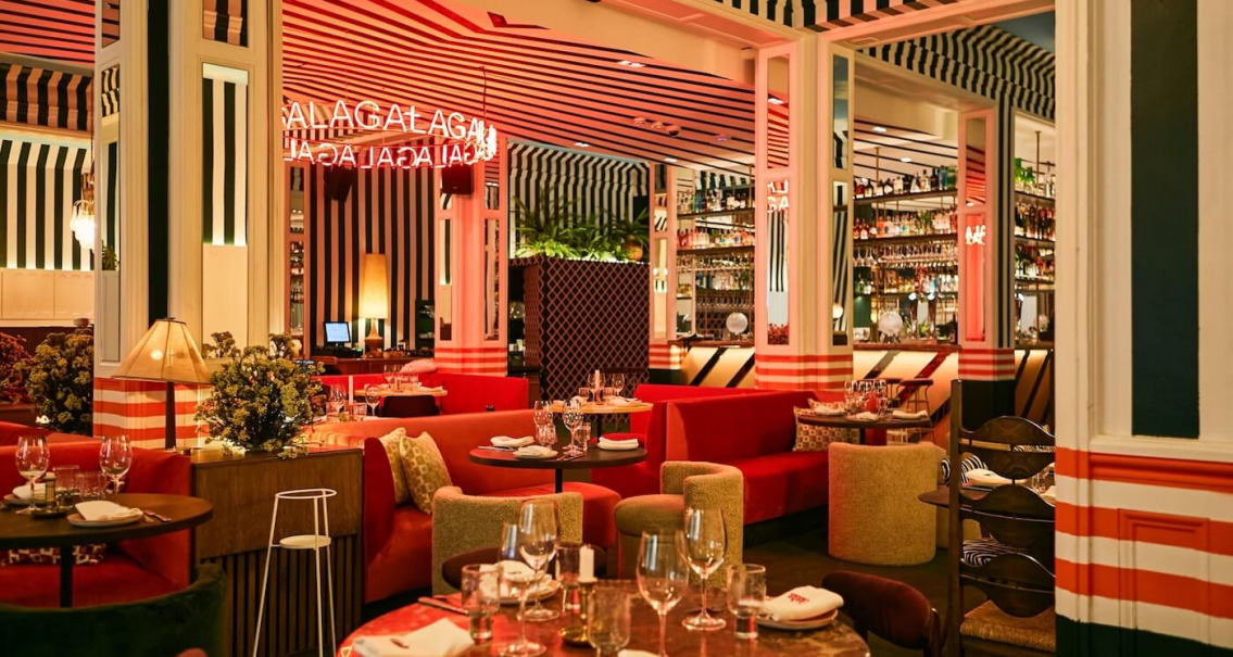 Zona de comedor del restaurante Gala con sofás tapizados, barra retroiluminada, neón decorativo y diseño escenográfico.