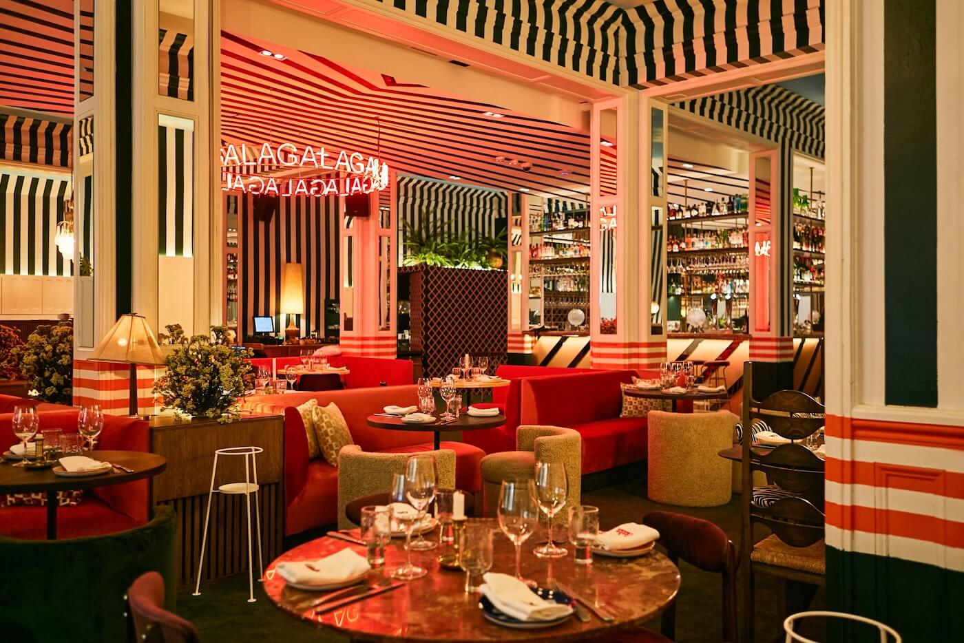 Zona de comedor del restaurante Gala con sofás tapizados, barra retroiluminada, neón decorativo y diseño escenográfico.