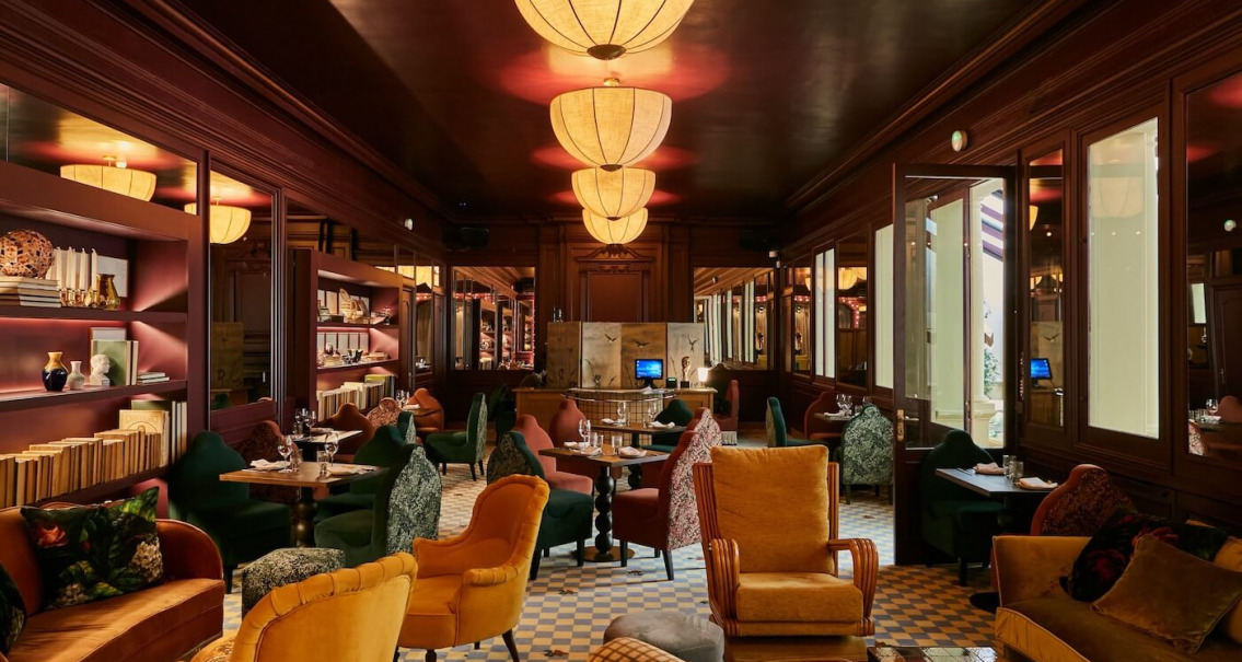 Salón del restaurante Gala con decoración de inspiración club, mobiliario vintage colorido e iluminación cálida.