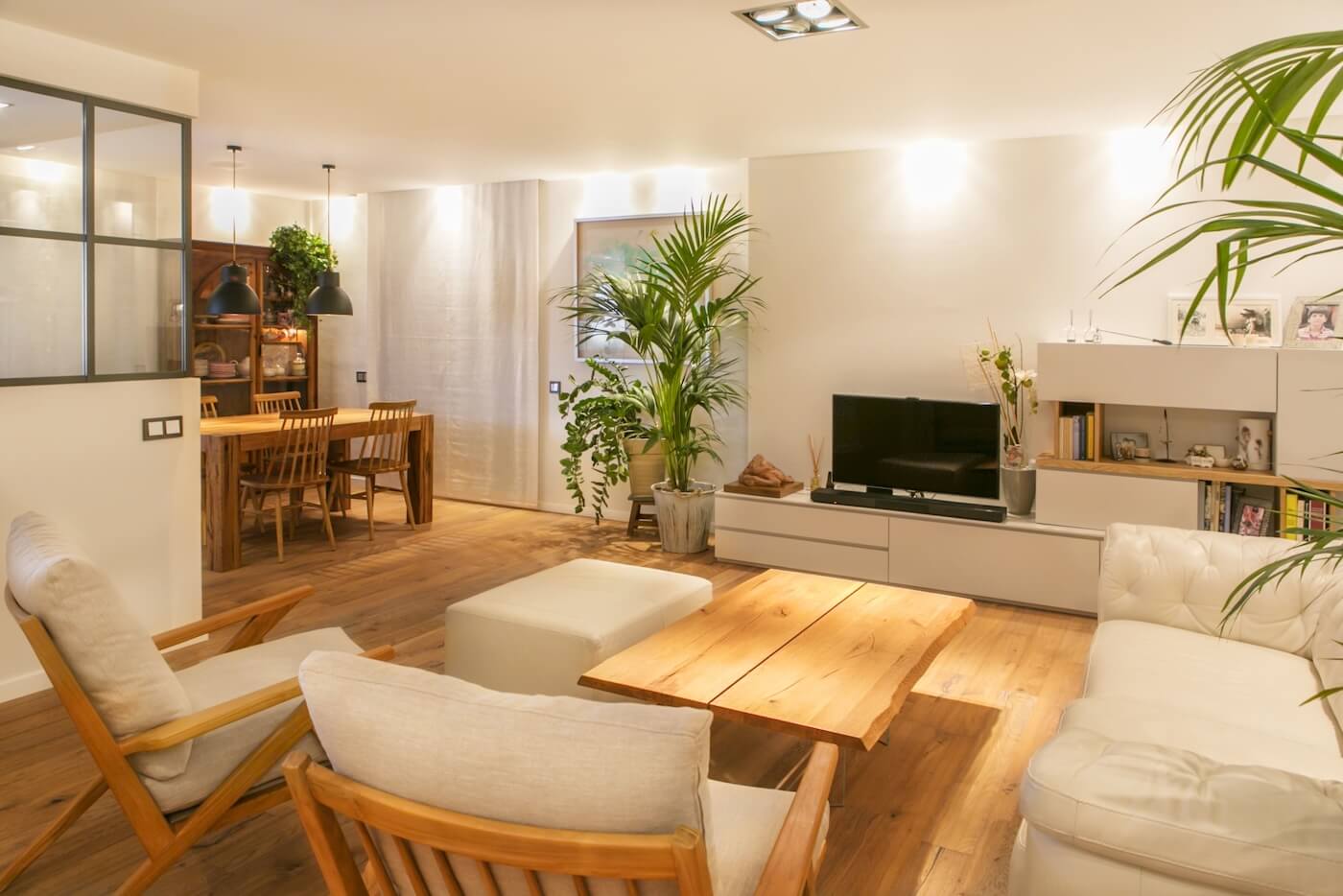 Salón comedor reformado con suelo de madera, mobiliario natural, iluminación cálida y decoración vegetal en vivienda de Sabadell.