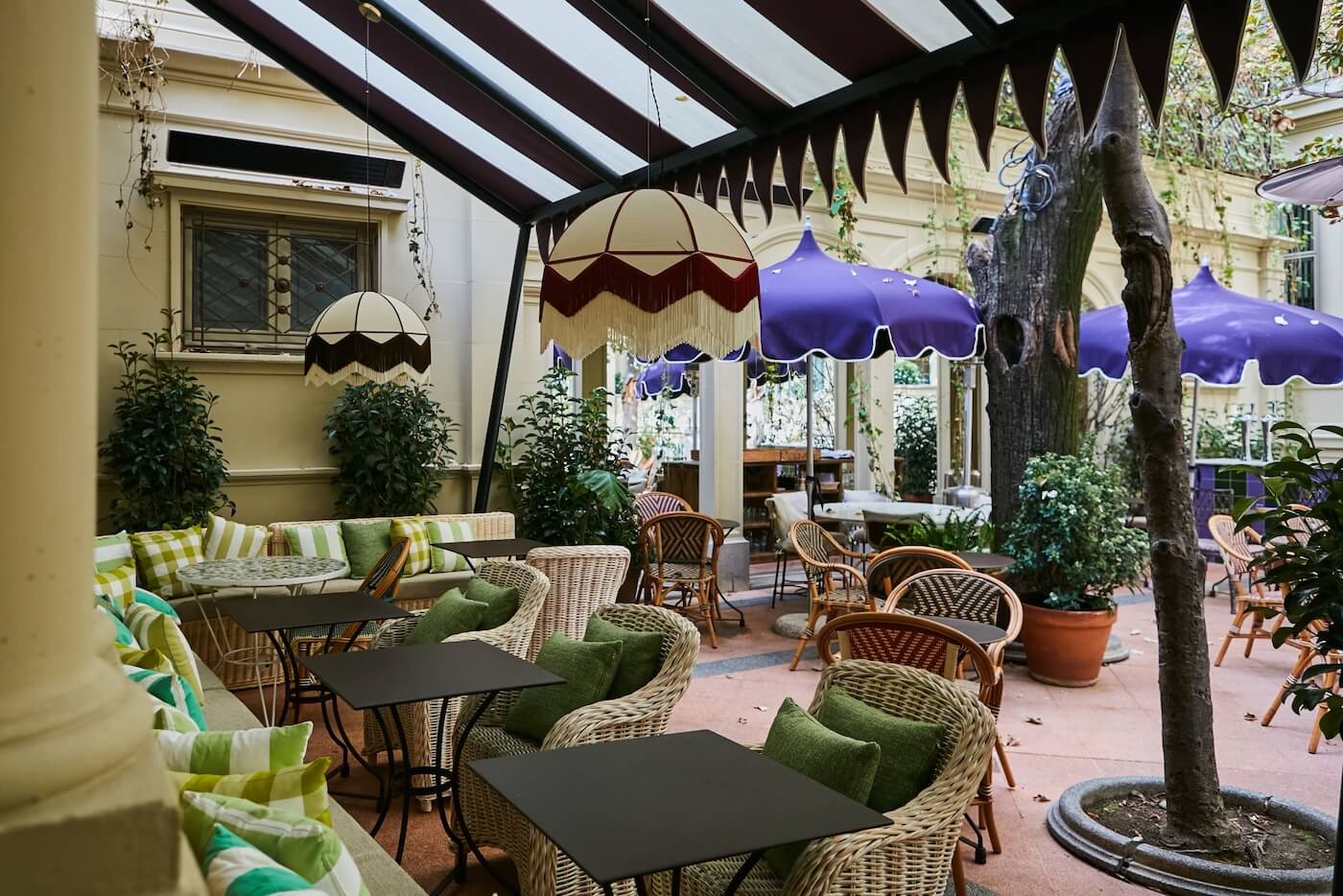 Terraza del restaurante Gala con mobiliario de fibras naturales, sombrillas moradas y luminarias decorativas con flecos.